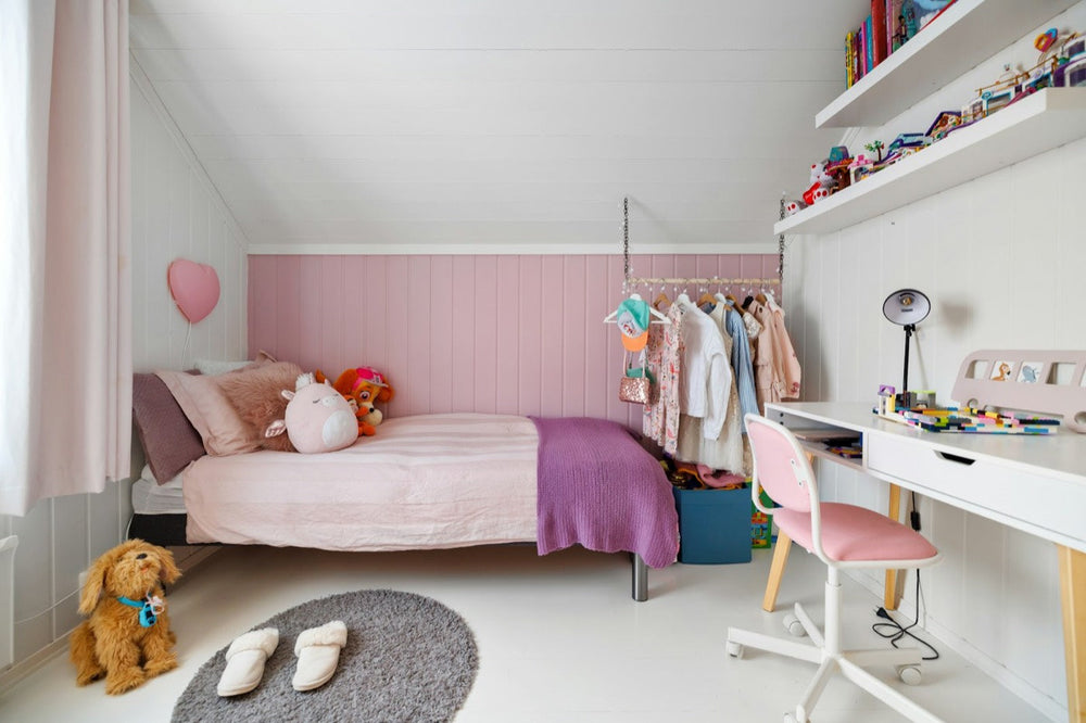 Bright Scandinavian kids' bedroom with pink wall panelling, a bed with pillows and soft toys