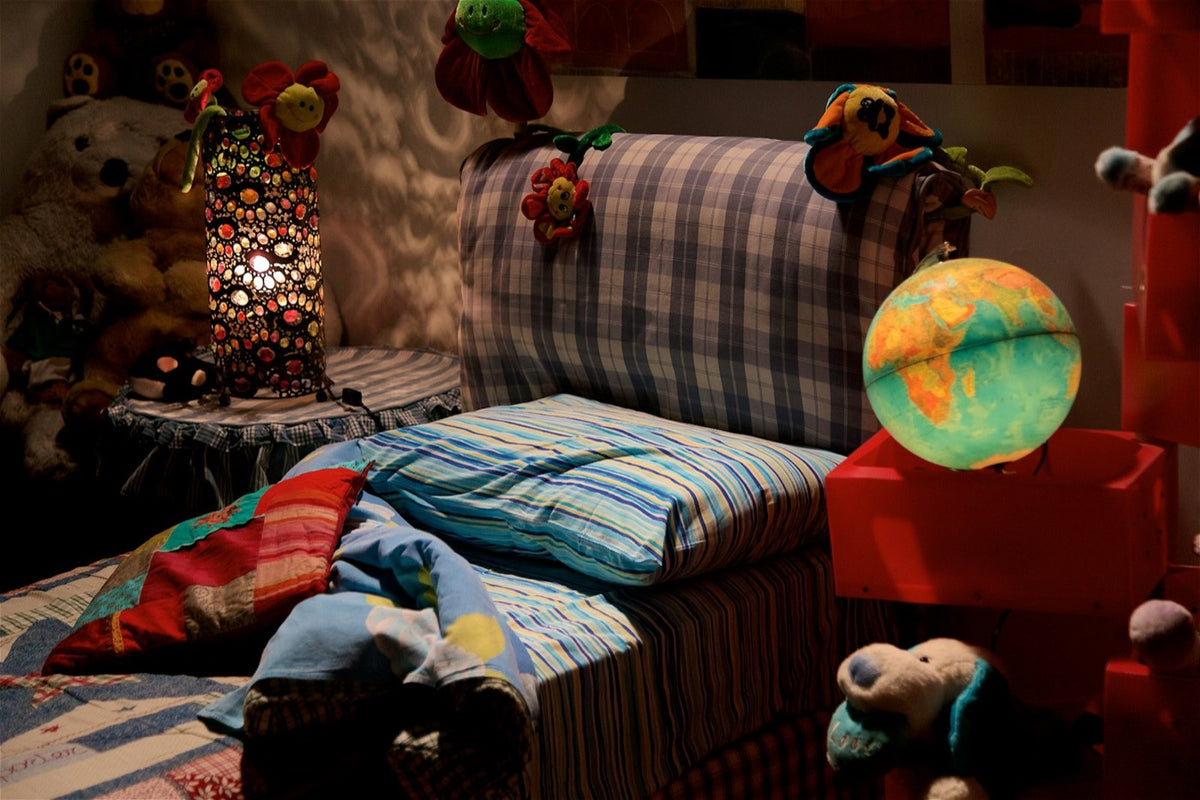 Colourful kids' bedroom in the evening with a striped duvet, mosaic lamp, glowing globe and soft toys