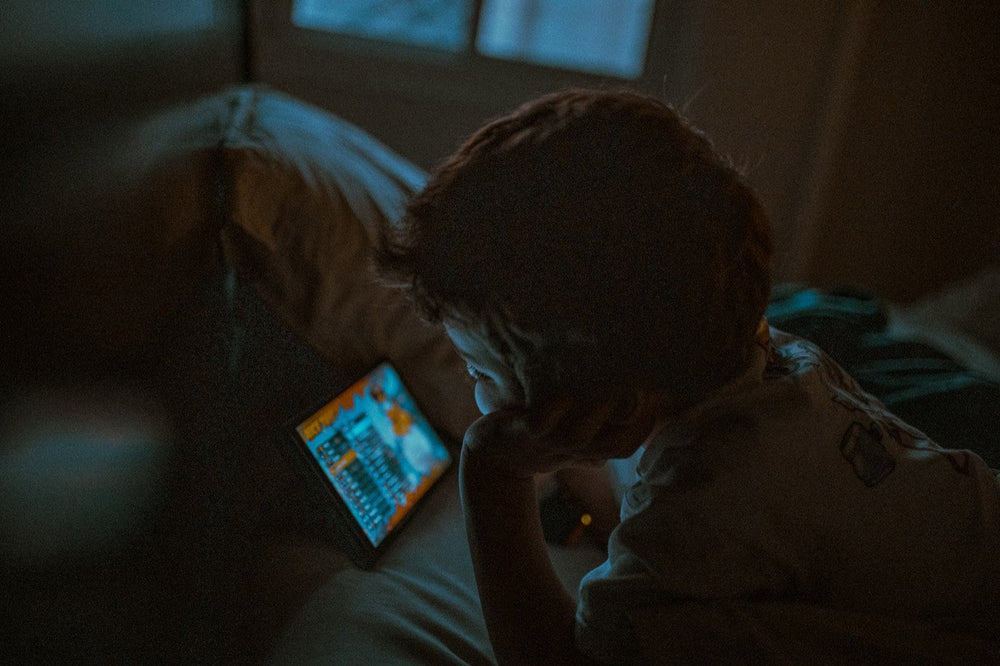Child lying in bed in a dark room watching a tablet