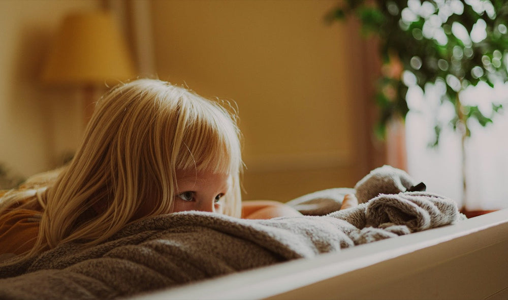 Little girl with a fringe resting under a soft blanket on the sofa, warm afternoon light and a lamp in the background