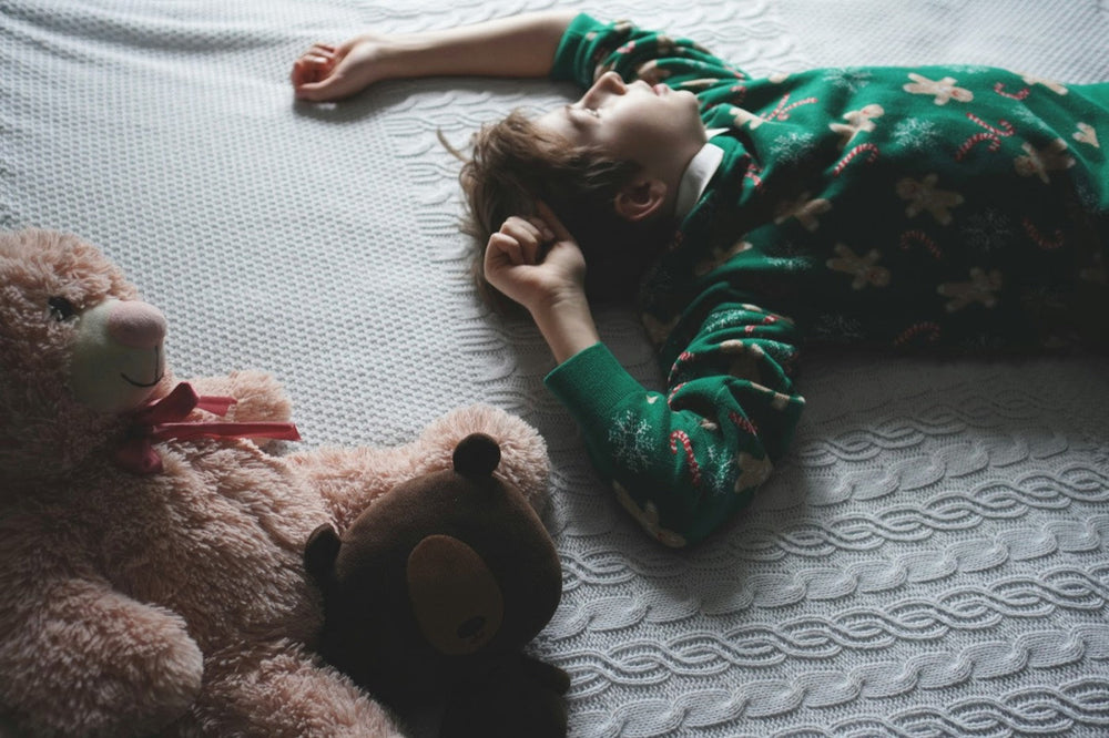 Little boy in green pyjamas lying on the bed next to two teddy bears